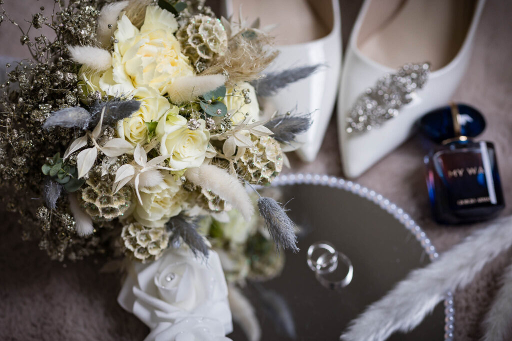 Detailnahaufnahme aller Accessoires von der Hochzeit in Fahlenbach beim Getting Ready. Brautschuhe, Parfüm, Eheringe, Spiegel und Brautstrauß