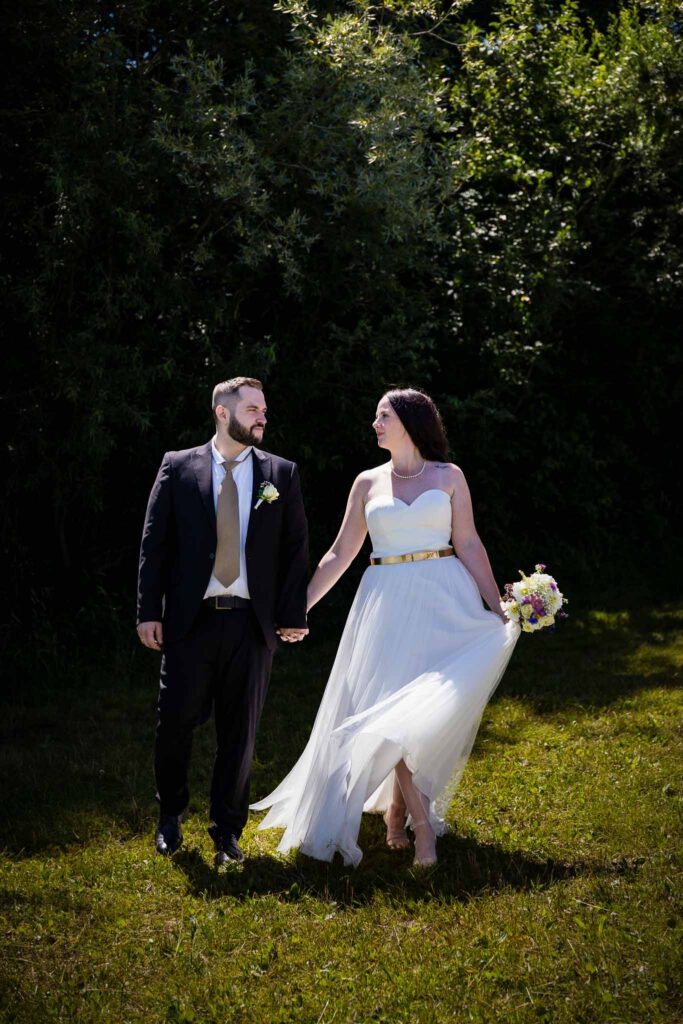 Pia und Marcel gehen beim Brautpaarshooting Hand in Hand am Höglinger Weiher.