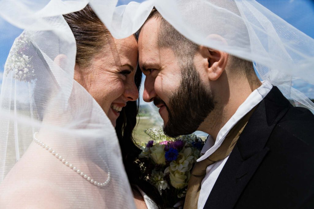 Pia und Marcel unter dem Schleier mit den Hochzeitsfotografen München sie lachen sich verliebt an.