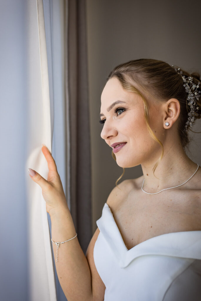 Ein nachdenklicher Blick vorbei am Vorhang von unserer Braut Julie beim Getting Ready auf der Hochzeit in Wolnzach