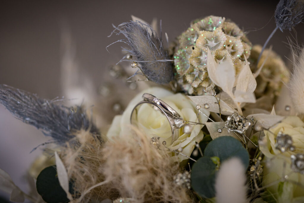 Die Ringe in Nahaufnahme mit Blumen im Hintergrund – ein Blick fürs Wesentliche vom Hochzeitsfotograf Rohrbach.
