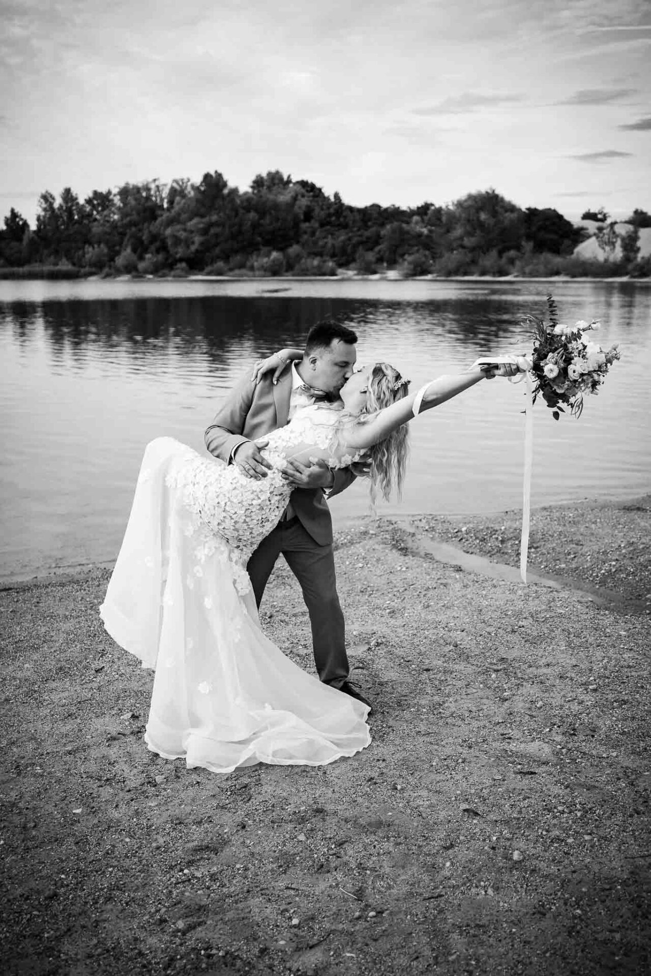 Dip Kiss vom Brautpaar in schwarz weiß vor dem Pucher Meer in Fürstenfeldbruck