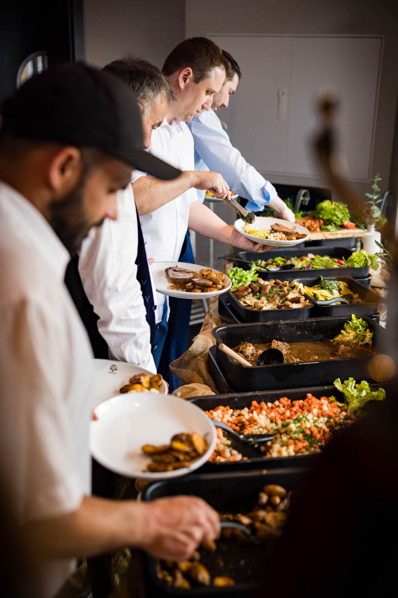 Die Gäste stehen am großen Buffet an mit Fokus auf das Buffet selbst die Gäste sind leicht unscharf im Bokeh zu sehen