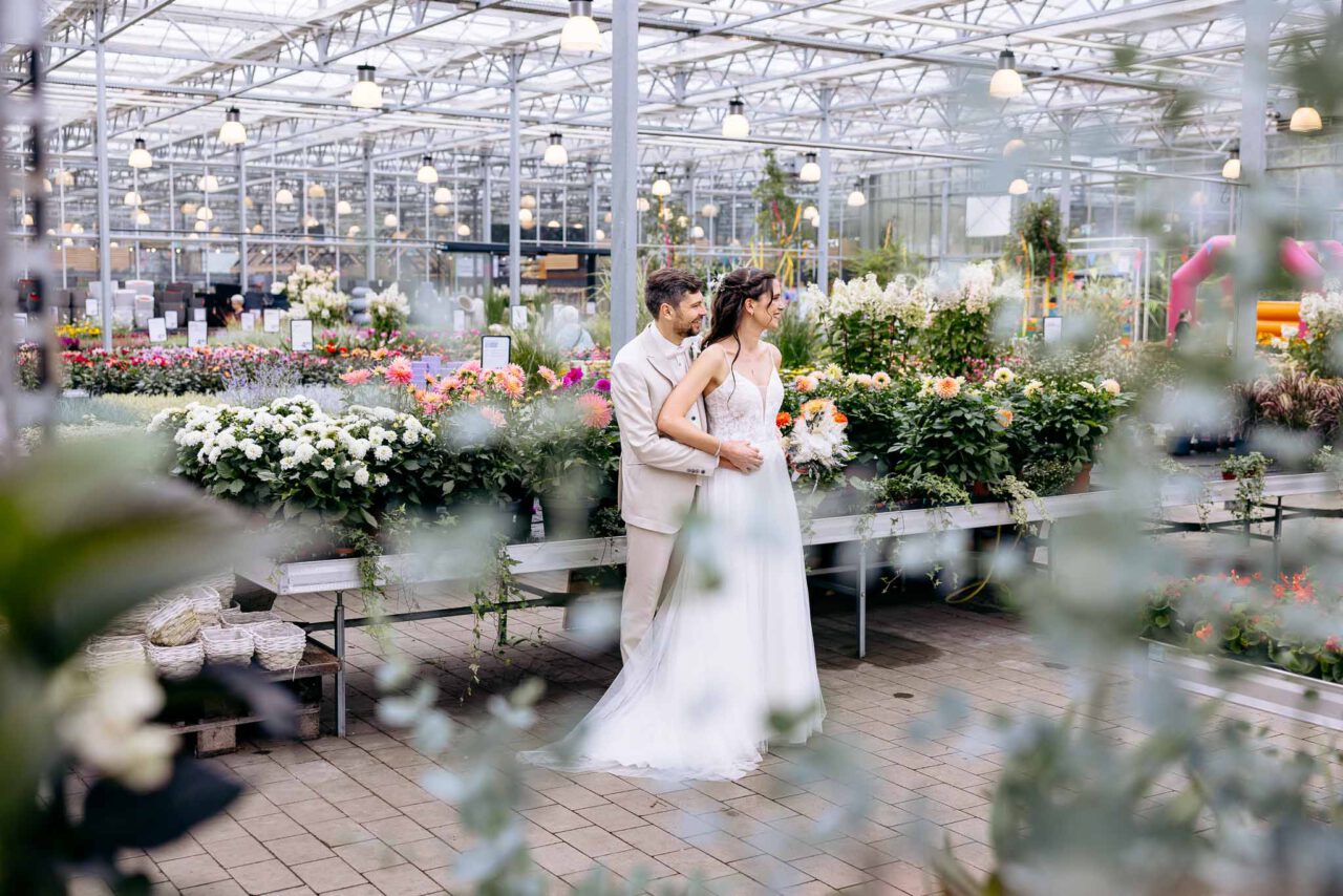 Weitwinkelaufnahme vom Brautpaar im Gartencenter Kiefl beide blicken nach rechts in die Ferne