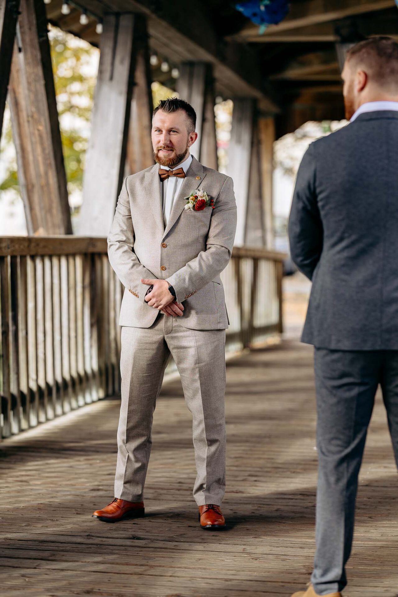 Der Bräutigam steht bereit zum First Look mit seiner Braut in Wolfratshausen auf der hölzernen Brücke
