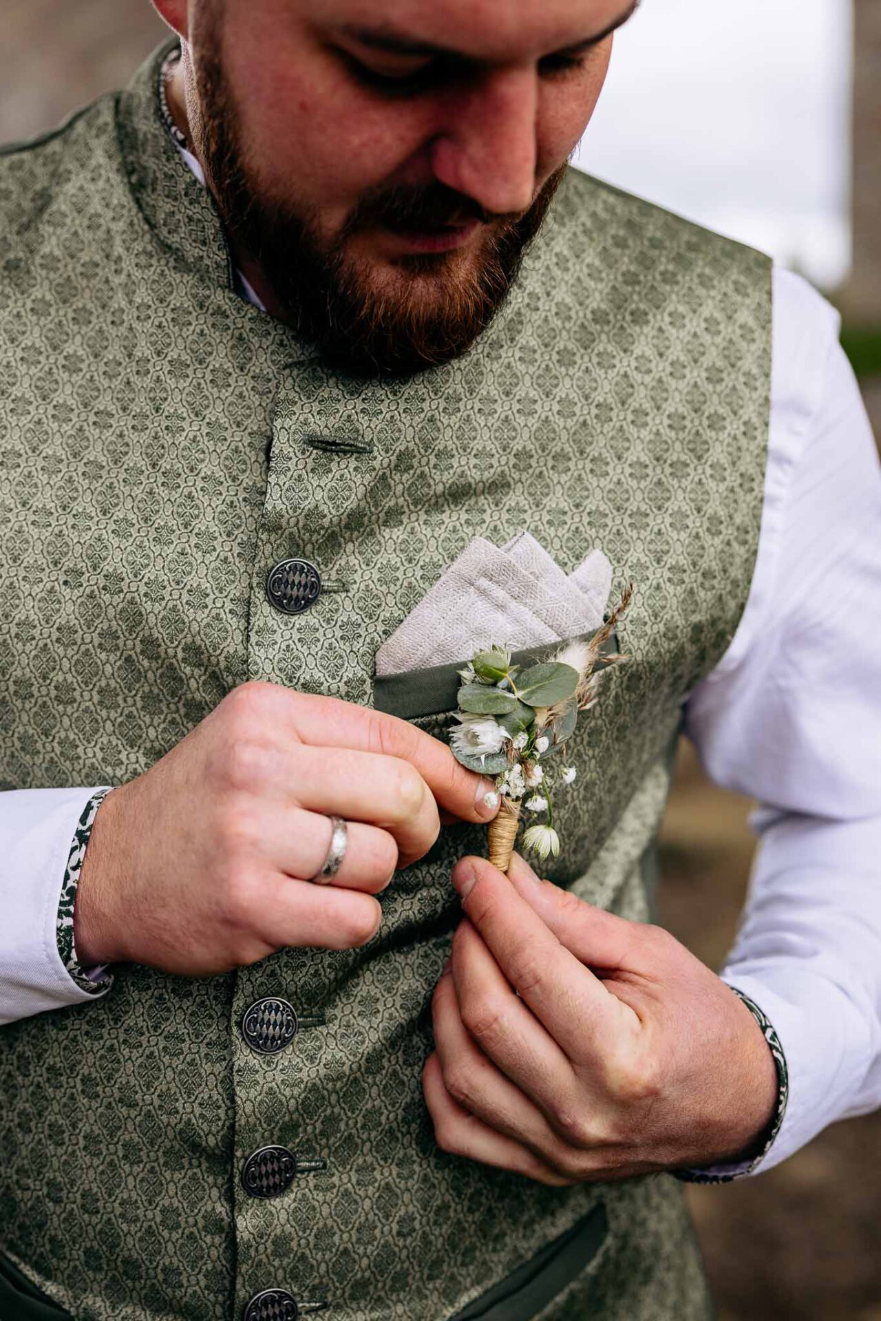 Bräutigam Michael richtet seinen Anstecker an seiner Trachtenweste hin