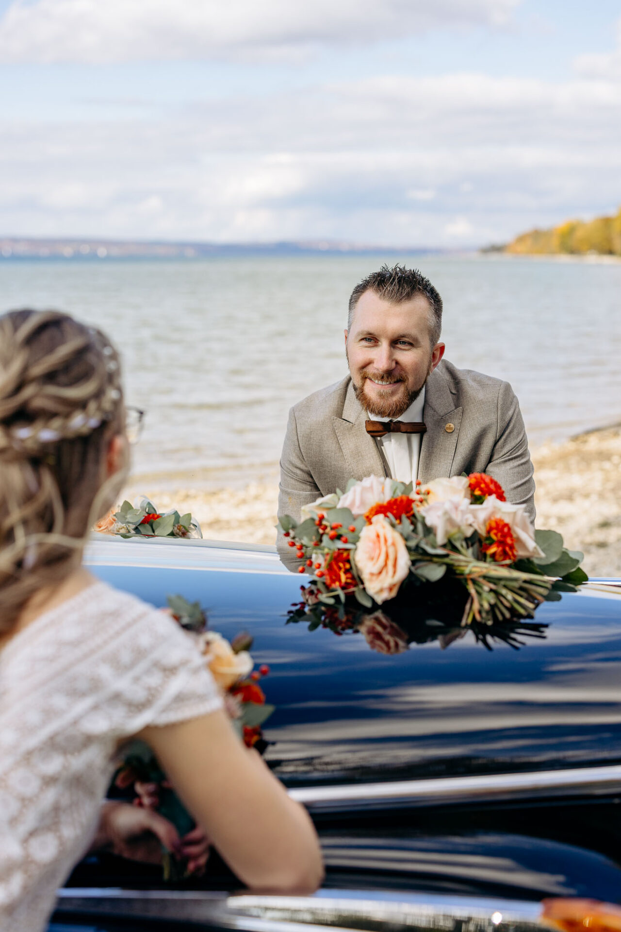 Das Brautpaar lehnt auf ihrem Hochzeitsauto am Starnberger See