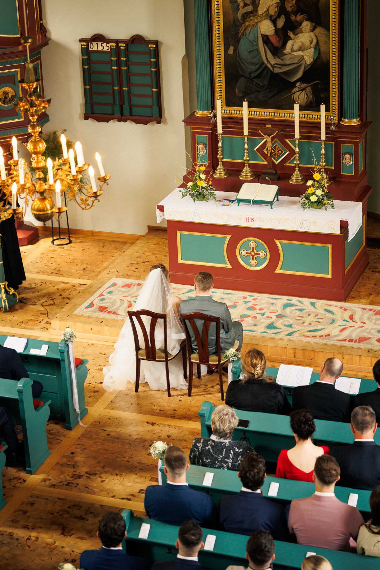 Das Brautpaar sitzt vor dem Altar während der Pfarrer die Traurede hält